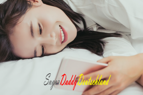 Mädchen schaut glücklich auf das Handy, das auf dem Bett liegt