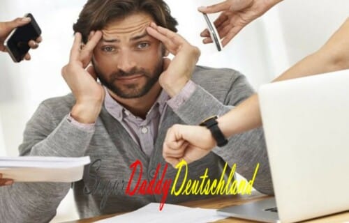 Un hombre ocupado con teléfonos alrededor de su portátil se toca la cabeza con gesto cansado.